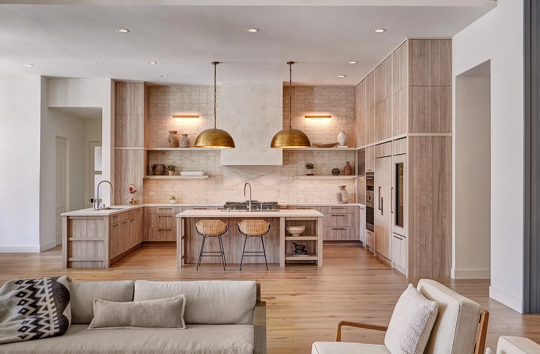 Pale wood cabinetry, sculptural brass pendants, and a stone island in the California Dream kitchen