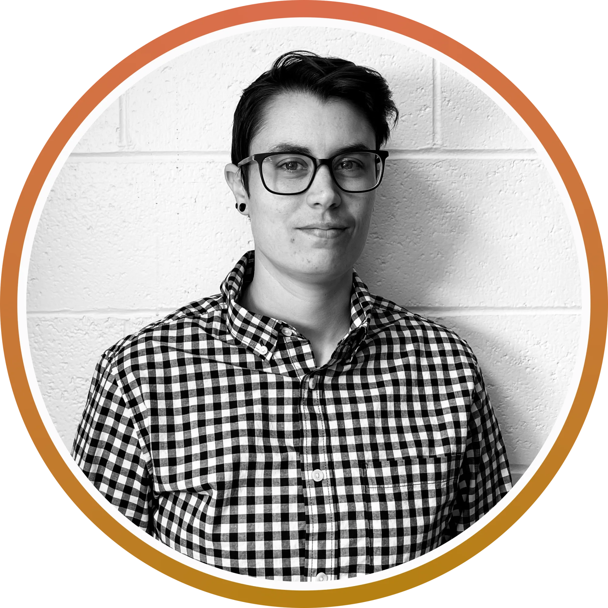 Black and white portrait of a person with short dark hair, glasses, and a checkered shirt, standing against a textured wall.