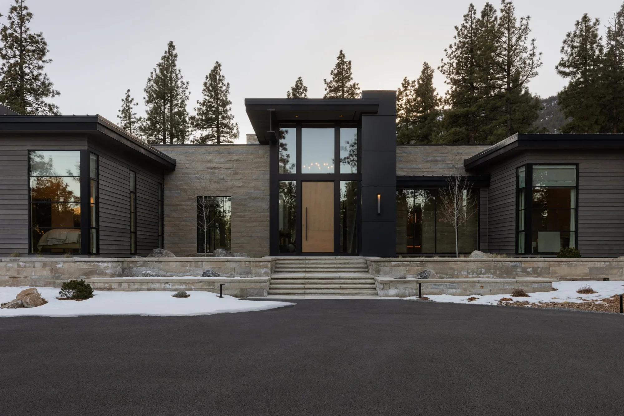 Mountain modern new construction home exterior, dark wood siding, tall glass entry