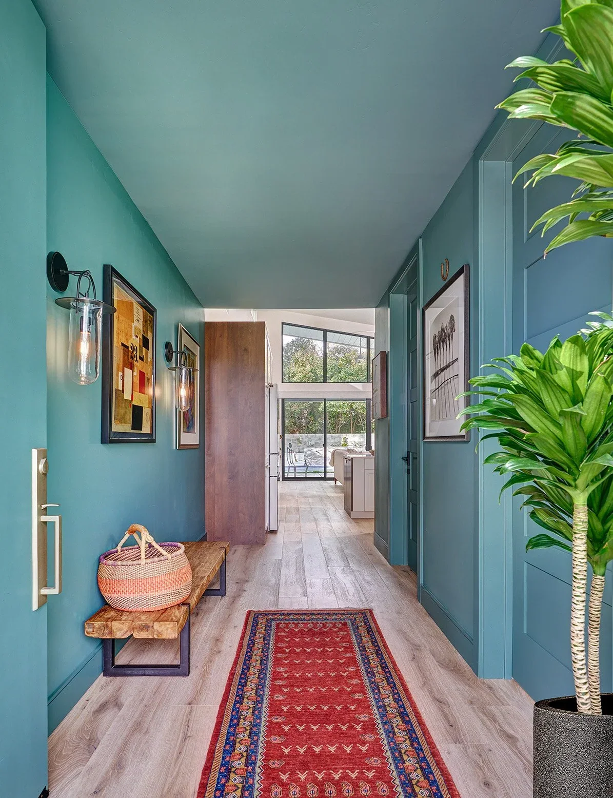A vivid teal entry with collected art, a woven rug, and a view through the Rake ADU