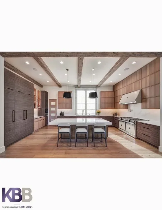 Modern open-concept kitchen with wooden cabinets, large island, black pendant lights, stainless steel appliances, and wooden flooring.