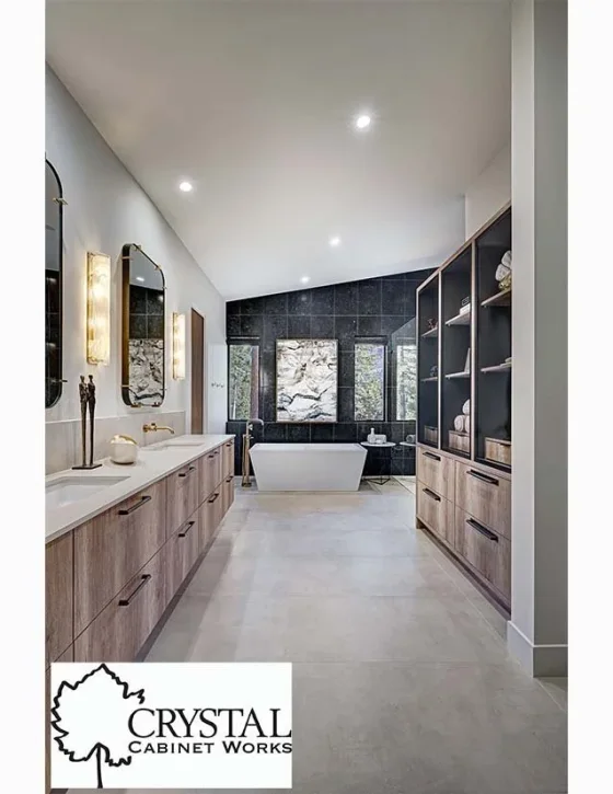 Modern bathroom with a freestanding bathtub, black tiled accent wall, and large windows, with wooden cabinetry and decor.