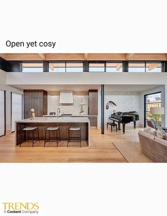Open-concept living space with kitchen island, bar stools, grand piano, and sitting area with a sofa, featuring modern decor and large windows.