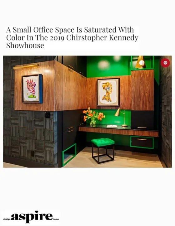 Small office space with wood paneling and green accents, featuring two colorful framed abstract art pieces, a green cushioned stool, a green lamp, and a vase with orange flowers.