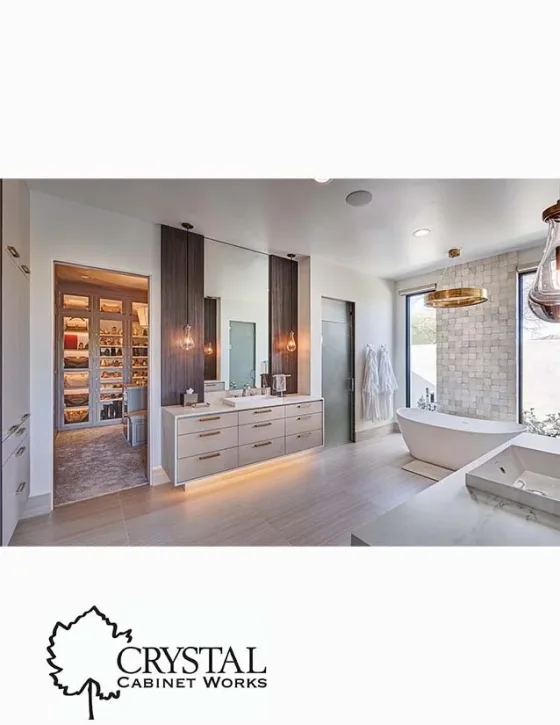 Modern bathroom with white walls, a bathtub near a window, a double vanity with two mirrors, pendant lights, and a walk-in closet with built-in shelves.