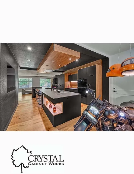 Modern kitchen with black and wood cabinets, island with built-in shelves, and a motorcycle parked nearby.